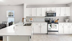 A modern kitchen with white cabinetry, a stainless steel stove, and a microwave.