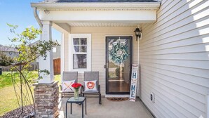 A house with a porch, two chairs, a small table, a stone pillar, and a wreath on the door.
