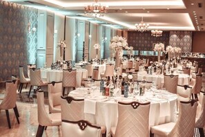 Een balzaal met ronde tafels, witte tafelkleden en bloemstukken.