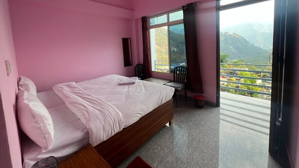 Un dormitorio con temática rosa, una cama, un ventilador de techo, una ventana con vistas a montañas y un balcón.