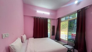 Una habitación rosa con una cama, una silla, un ventanal y un cubo de basura azul.