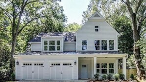 Ein zweistöckiges Haus mit Garage, einer überdachten Veranda und einem großen Baum im Hintergrund.