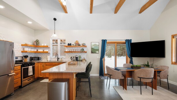 A modern kitchen with a central island, built-in appliances, and a dining area with a TV. - Northern Escape - Hot Tub, Sauna, Cold Plunge (Lake Ann)