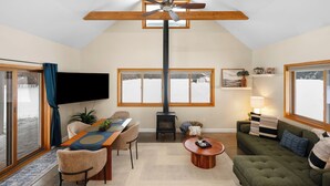 A cozy living room with a fireplace, a dining area, and a television mounted on the wall. - Northern Escape - Hot Tub, Sauna, Cold Plunge (Lake Ann)