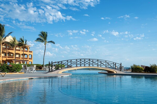 Une piscine avec un pont, des palmiers et un bâtiment doté de balcons.