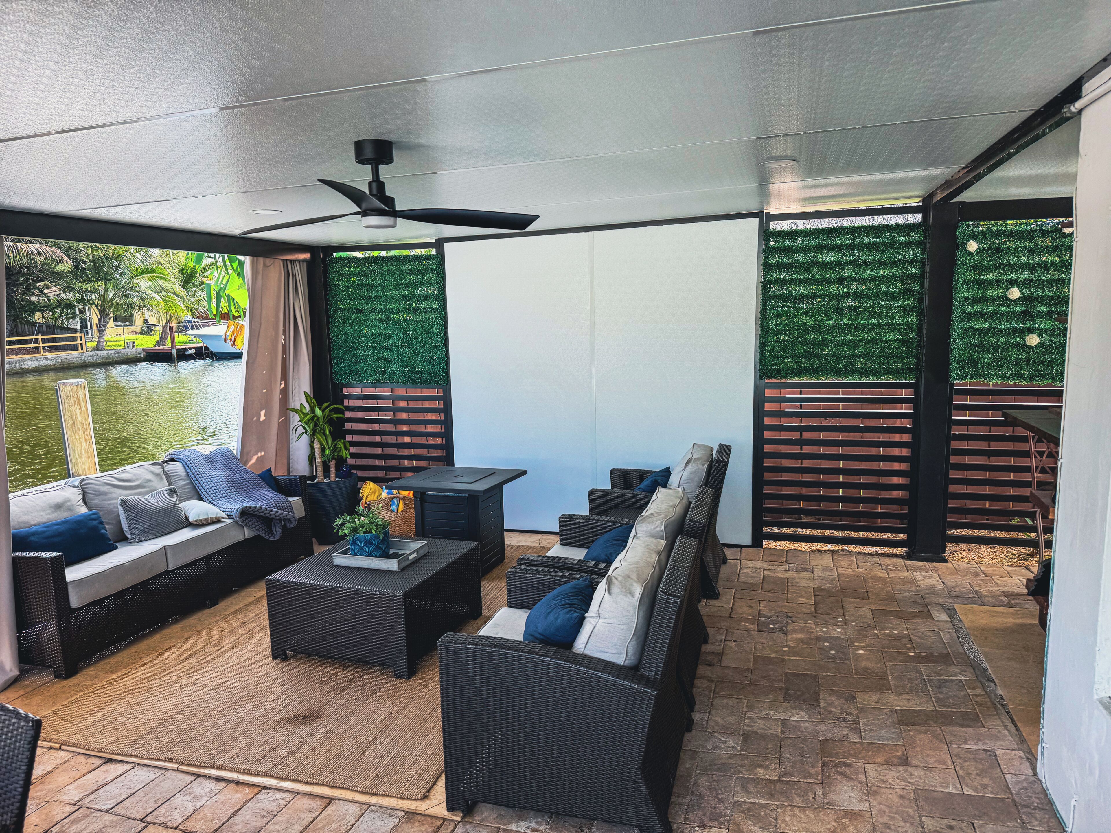 Eine Terrasse im Freien mit Korbmöbeln, einem Deckenventilator und Blick auf ein Gewässer.