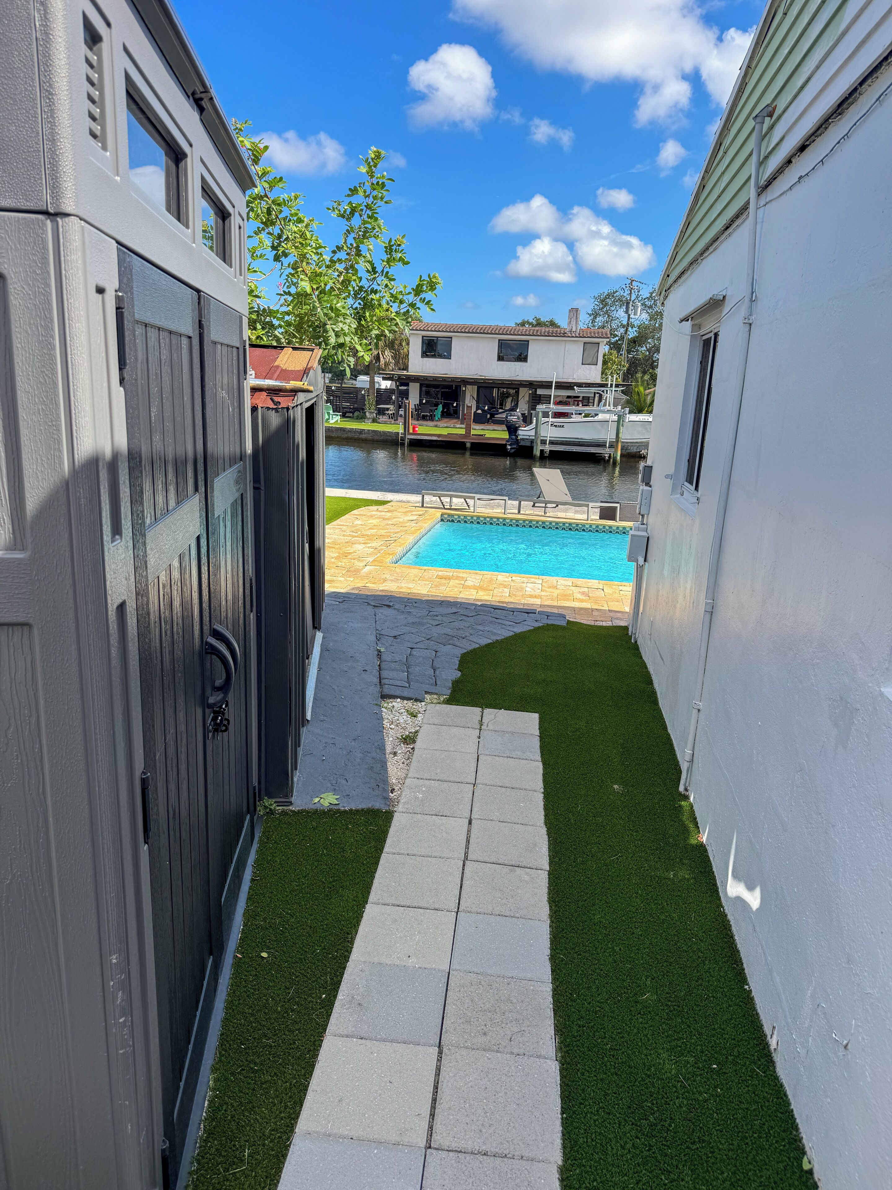 Un patio trasero con piscina, un camino pavimentado y un muelle para barcos.