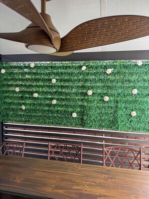 Ein Deckenventilator, eine grüne Wand mit weißen Rosen und eine Holzbank.