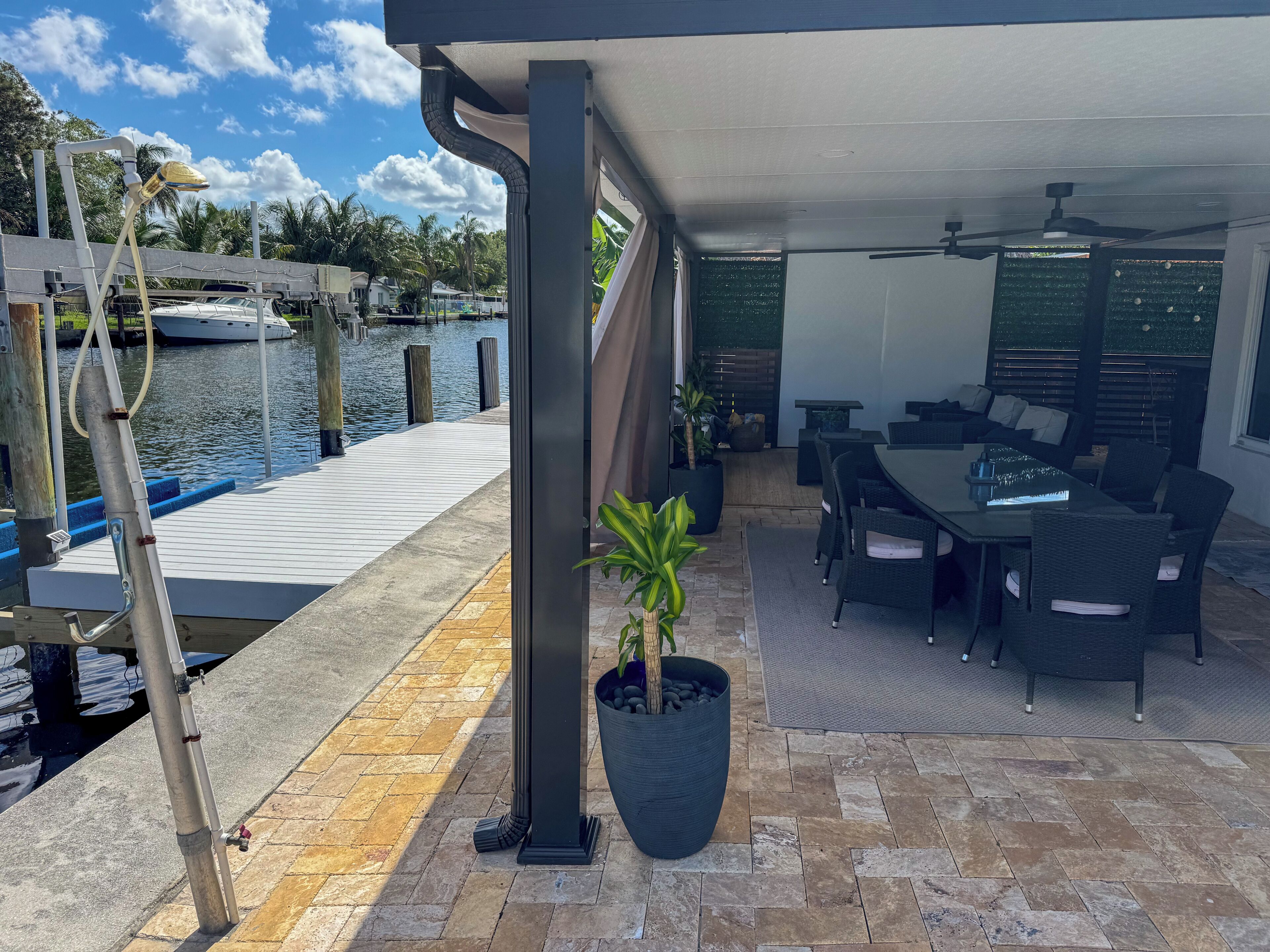 A covered outdoor area with a dining table and chairs, a potted plant, and a view of the water.