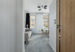 Ein modernes Interieur mit grauem Boden, einem weißen Sofa, einem Esstisch und Blick auf Gebäude durch große Fenster.