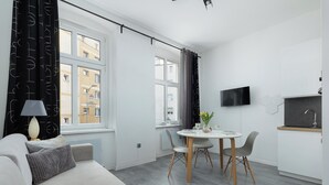 Moderni olohuone, jossa on sohva, ruokapöytä tuoleineen, seinälle asennettu televisio ja ikkuna, jossa on verhot.