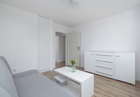 A modern, minimalist room with a grey sofa, a white desk, and a wardrobe.