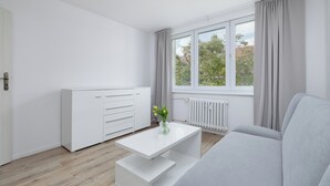 Ein modernes Zimmer mit einem weißen Sofa, einem weißen Couchtisch, einem weißen Schrank und einem Fenster mit Vorhängen.