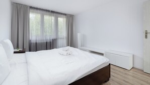 Ein modernes Schlafzimmer mit einem großen Bett, einem Nachttisch, einem Beistelltisch, einem weißen Kleiderschrank und transparenten Vorhängen.