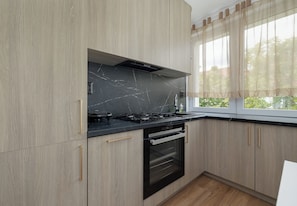 A modern kitchen with light wood cabinets, a black stove, and a built-in oven.