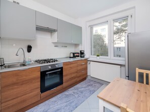 Una cocina moderna con estufa a gas, horno y lavaplatos, armarios de madera, un ventanal con vistas y una mesa de comedor de madera.