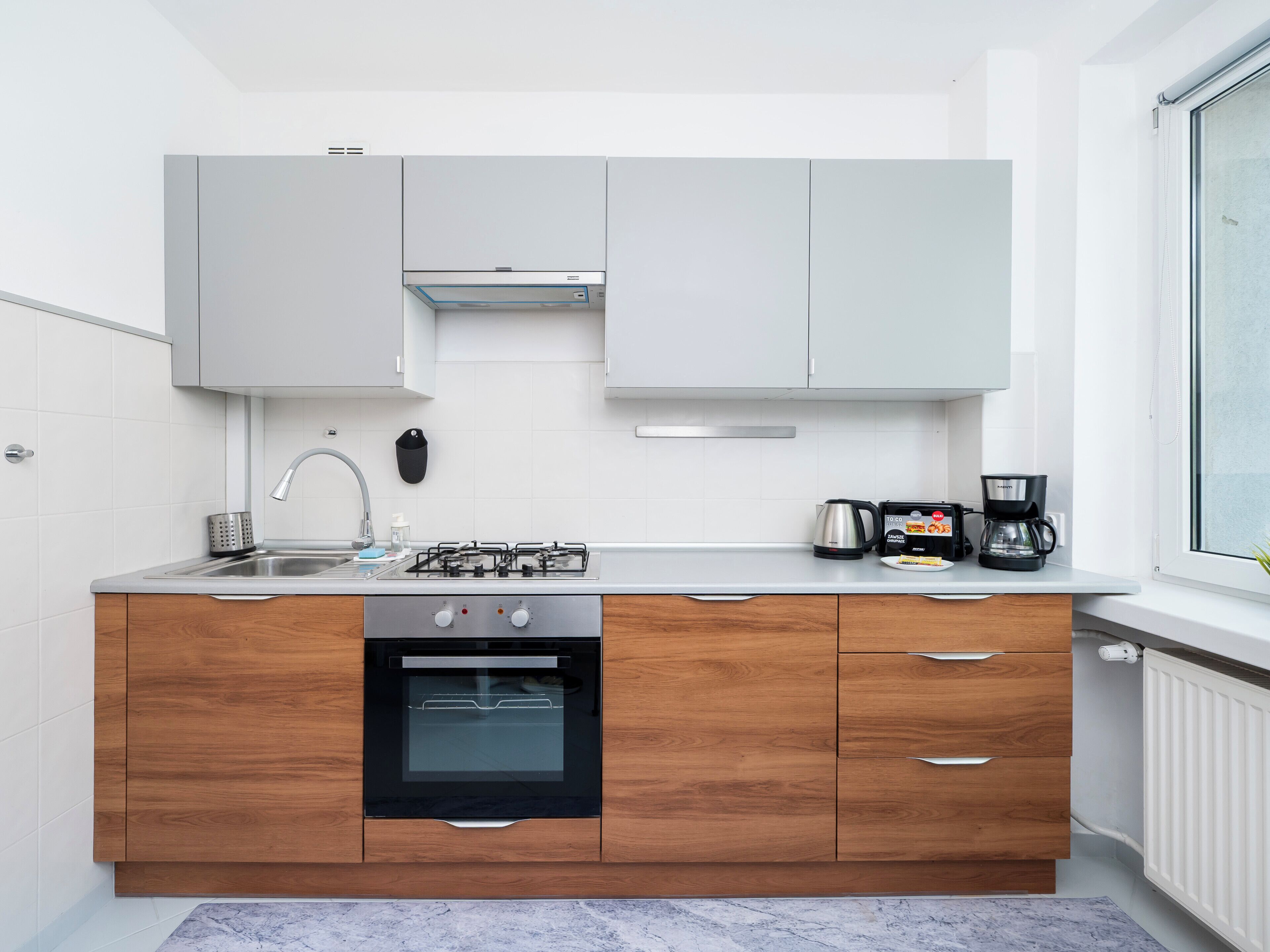 A modern kitchen with white cabinets, a built-in oven, a coffee maker, and a window.