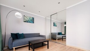 Ein modernes Wohnzimmer mit einem grauen Sofa, einem Holztisch und einem großen Spiegel, der einen weiteren Raum widerspiegelt.