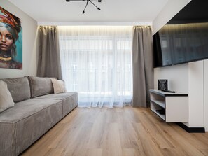 Ein modernes Wohnzimmer mit einer Couch, Vorhängen, einem Flachbildfernseher und Holzboden.