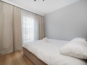 Ein Schlafzimmer mit einem Bett, einem Fenster mit leichtem Vorhangstoff und einer Leuchte.