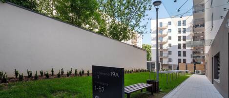 Un camino pavimentado, un banco, un cartel con números de apartamentos y un edificio con balcones.
