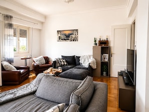 Un salon comprenant un canapé, des fauteuils, une table basse, un tableau, une bibliothèque et un téléviseur.