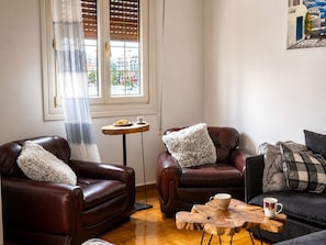 A living room with two brown leather sofas, a wooden coffee table, and a small round table with a plate of food and a cup.