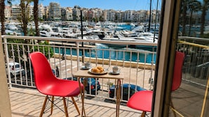 A balcony with two red chairs, a table with croissants and coffee, and a view of a marina with boats and buildings. - Your Stunning 2Bdrm, 2BA with Seaview in Pireaus (Pireas)