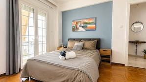 A bedroom with a bed, nightstands, a painting, a mirror, and a view through a window. - Your Stunning 2Bdrm, 2BA with Seaview in Pireaus (Pireas)