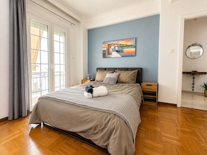 A bedroom with a bed, nightstands, a painting, a mirror, and a view through a window.