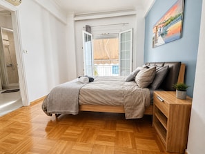 Une chambre à coucher avec un lit, une table de chevet, une plante en pot et une vue sur l’extérieur.