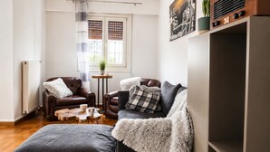A living room with a brown leather sofa, a grey ottoman, a small wooden coffee table, and a potted plant. - Your Stunning 2Bdrm, 2BA with Seaview in Pireaus (Pireas)