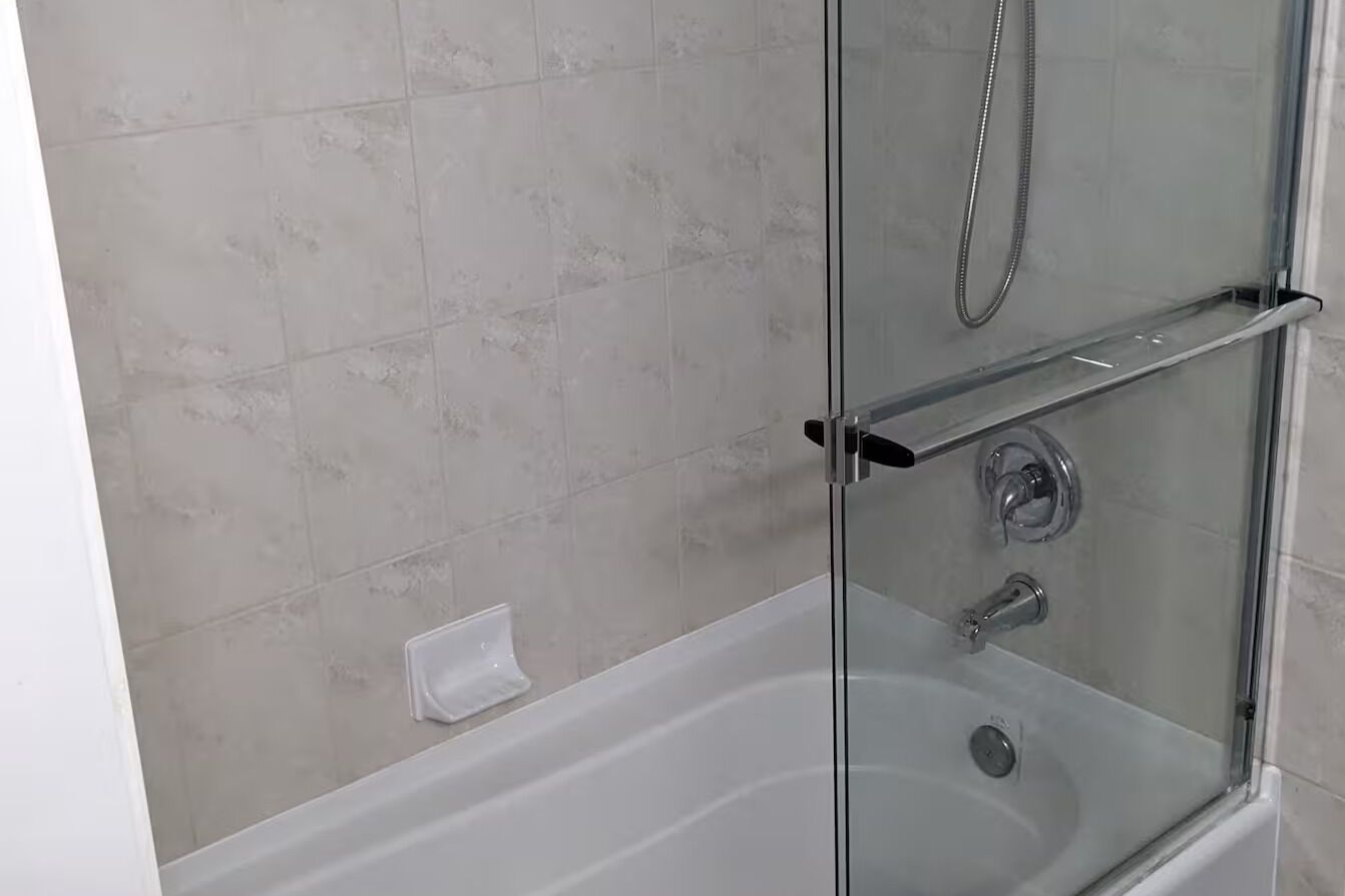 Ett duschutrymme med glasväggar, en handhållen duschslang, en kontrollpanel och en glashylla.