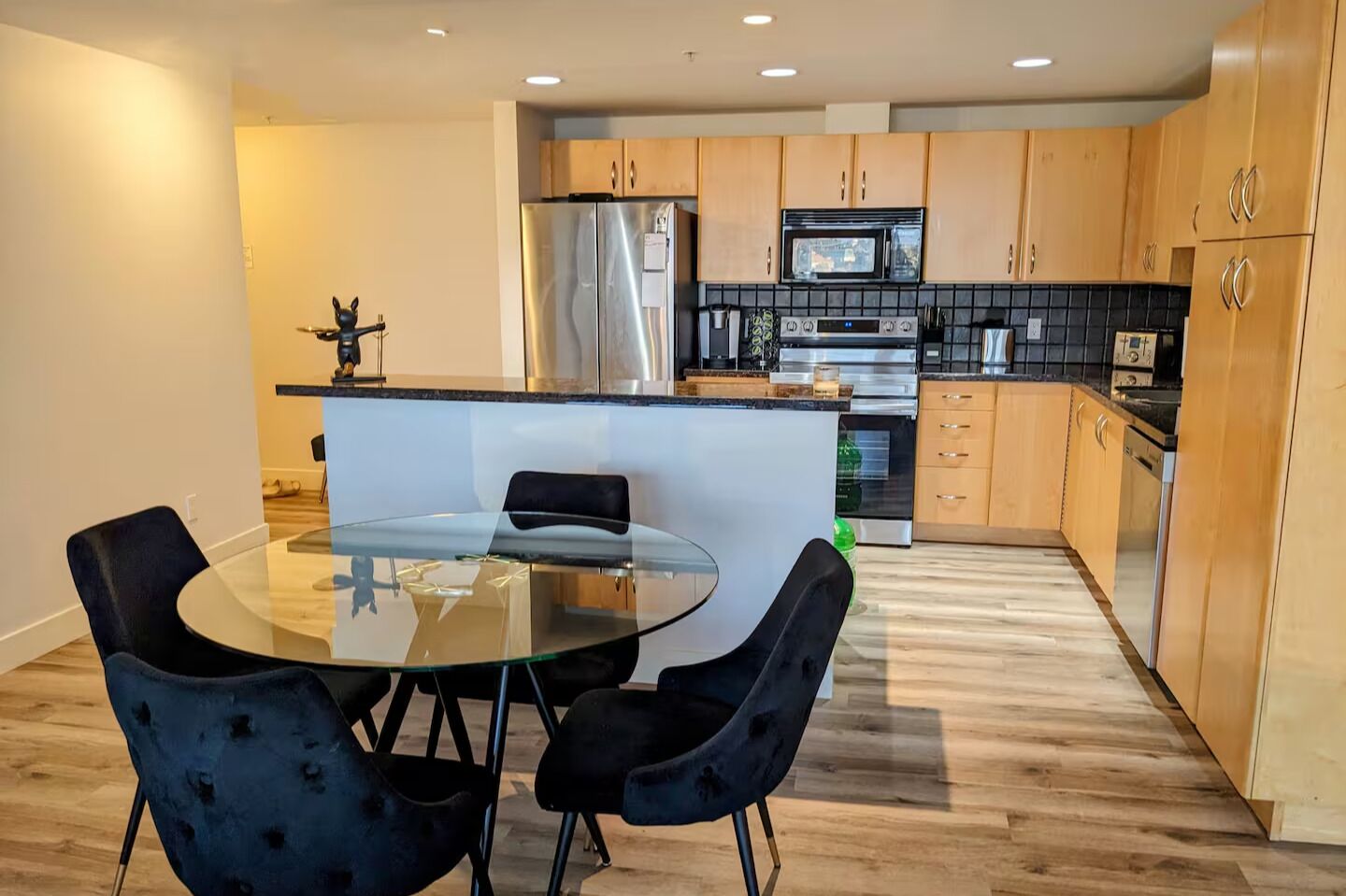 A modern kitchen with a central island, black chairs, and wooden cabinets.