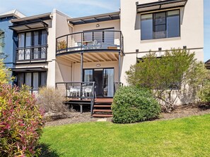 Een modern, twee verdiepingen hoog gebouw met een balkon, een klein terras en een verzorgd gazon.
