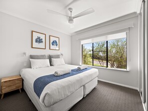 Ein Schlafzimmer mit einem großen Bett, einem Deckenventilator, einem Nachttisch, einem Fenster mit Aussicht und zwei gerahmten Bildern an der Wand.