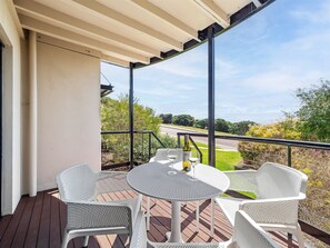 Een overdekt terras buiten met een tafel en stoelen, met uitzicht op een weg en groen.