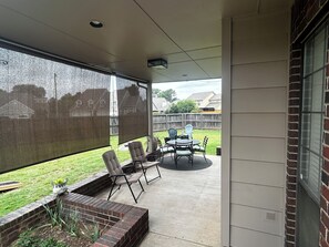 Une terrasse couverte avec un jardin en briques, du mobilier d’extérieur et une vue sur le jardin arrière.