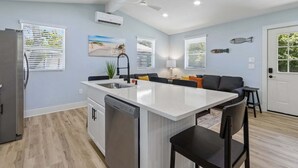 A modern kitchen with a central island, a refrigerator, a dishwasher, and a dining area with a sofa and chairs. - Sunset Drift Cottage (Fernandina Beach)
