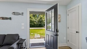 An open door leading to a grassy area, a gray sofa, and a small table. - Sunset Drift Cottage (Fernandina Beach)