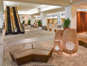 Eine Hotellobby mit einer zentralen Treppe, Sitzgelegenheiten, einer Rezeption und dekorativen Pflanzen.