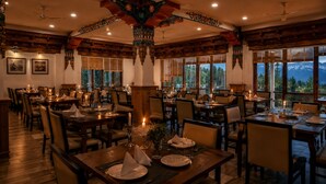 Un restaurante con varias mesas preparadas para comer, amplias ventanas con vista a la montaña y arquitectura de madera tradicional.