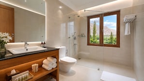Un baño moderno con lavamanos, inodoro, ducha y ventana con vista a la montaña.