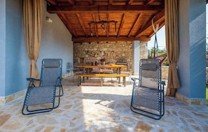 A covered outdoor seating area with stone flooring, a wooden table, and two chairs. - Holiday home with air conditioning and terrace (Galižana)