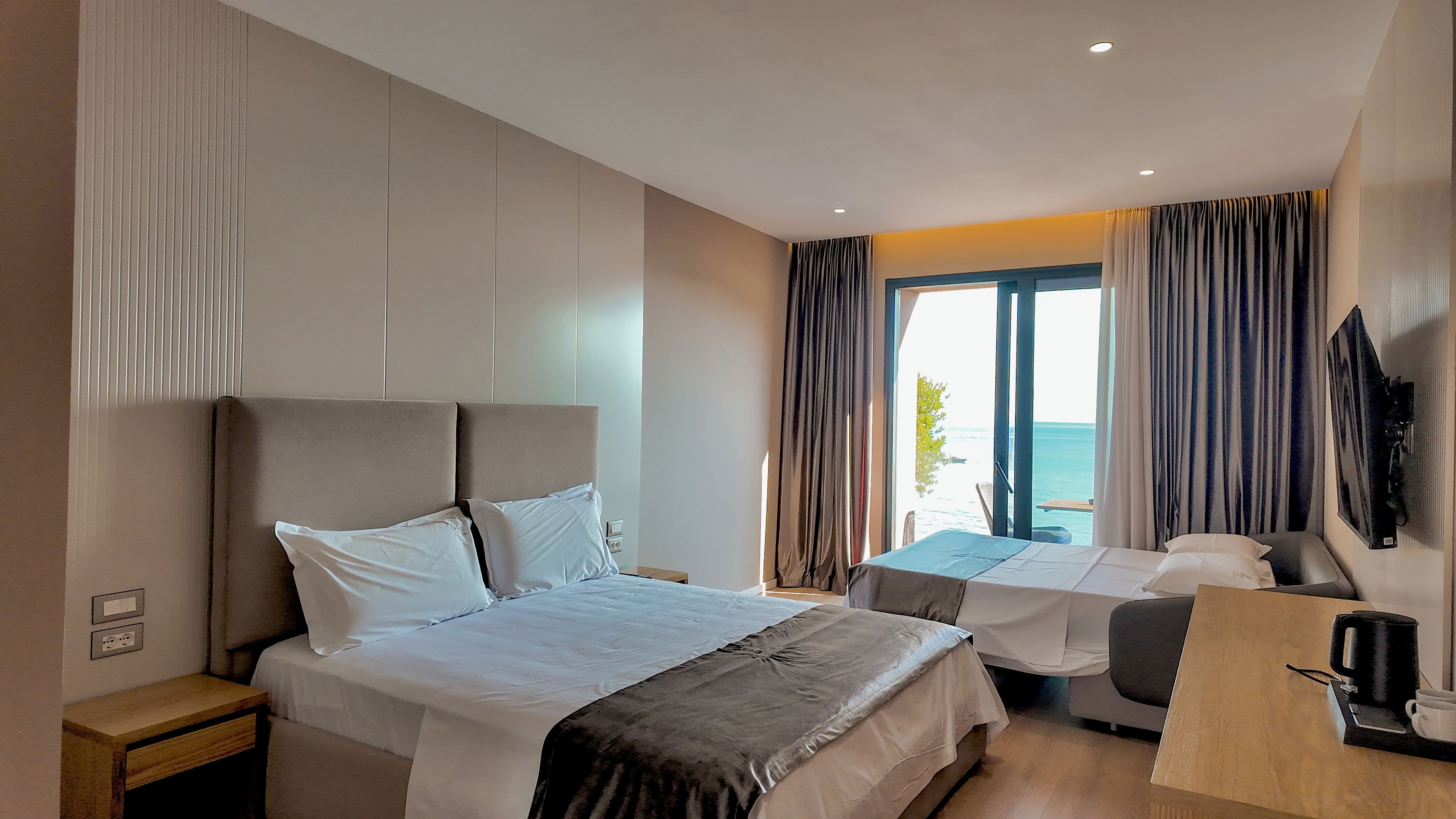 Habitación de hotel con cama, escritorio, silla, televisión y vista al mar.