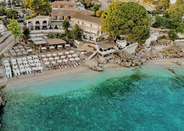 A coastal hotel with multiple balconies, beachside seating, and a clear view of the turquoise sea.