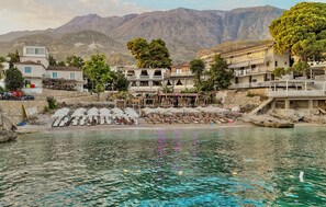 A coastal hotel with multiple balconies, a pool area, and a view of mountains in the background. - Hotel Platinium Dhermi (Dhermi)