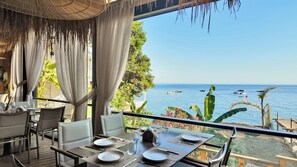 A dining area with a table set for two, overlooking a clear blue sea with boats.