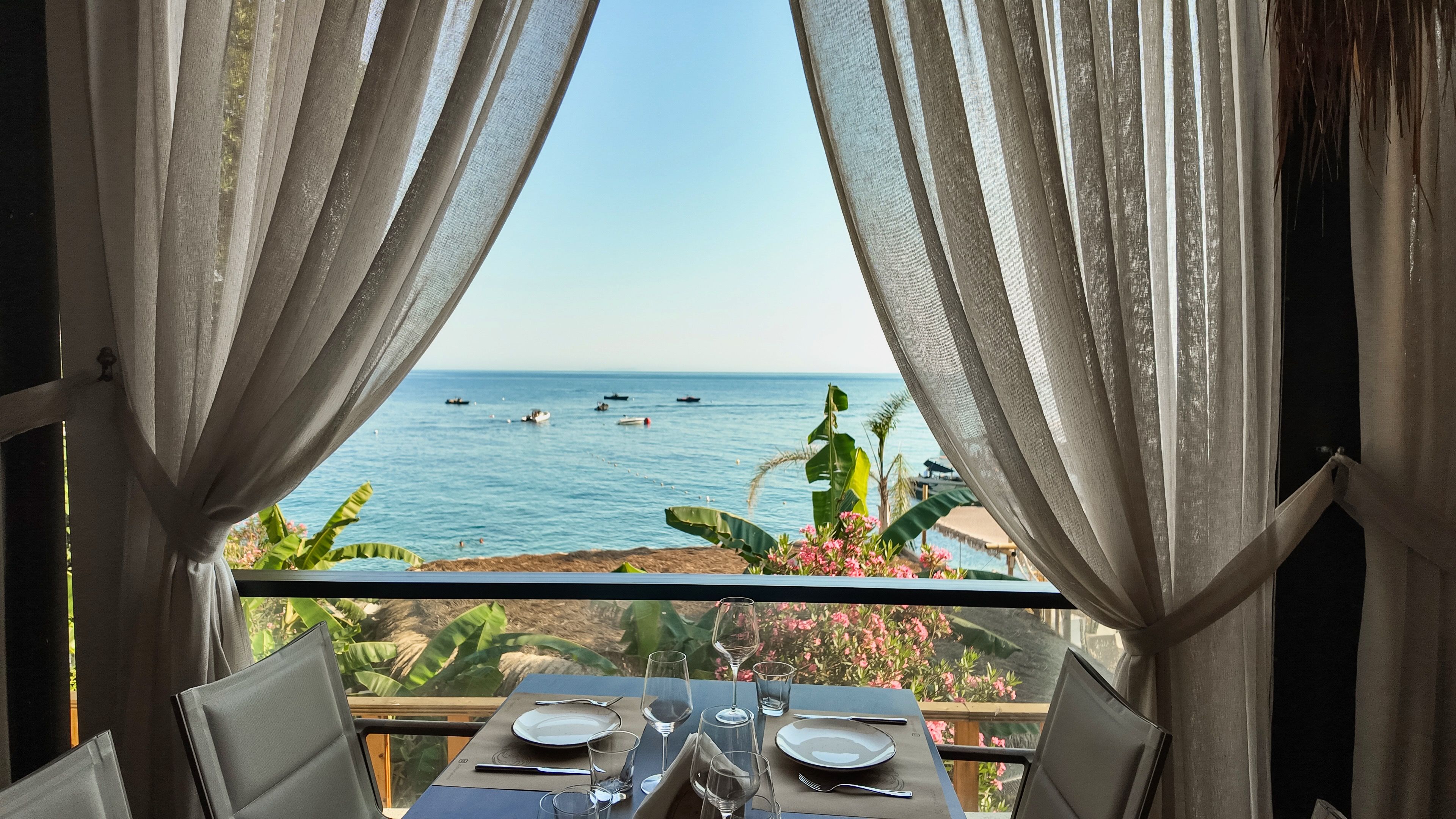 Mesa posta para refeição com vista para o mar e barcos.
