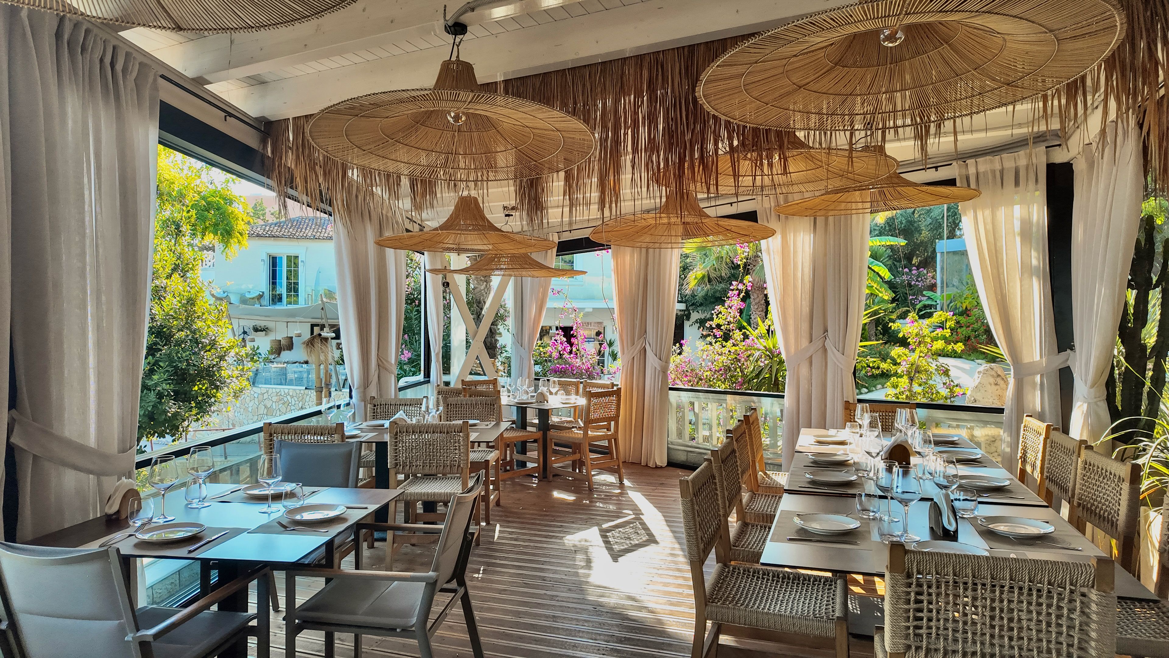 Un restaurante con mesas al aire libre, muebles de mimbre y sombrillas colgantes de ratán.